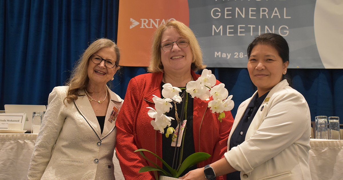 RNAO CEO Dr. Doris Grinspun (left) and outgoing RNAO President NP Lhamo Dolkar (right) welcome new RNAO President Sue LeBeau with smiles and an orchid at the 101st RNAO AGM on May 29, 2026.  