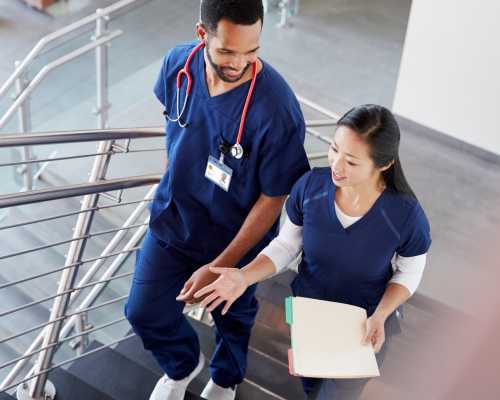 Two nurses talk while walking down stairs.