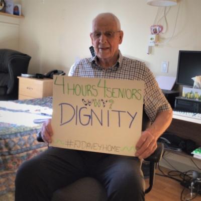 Long-term care resident in his room holding a sign asking for more care