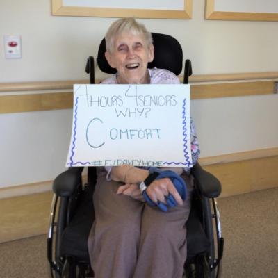Long-term care resident in her room holding a sign asking for more care