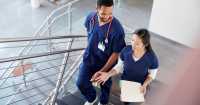 Two nurses talk while walking down stairs.