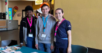 Three students stand at an RNAO table